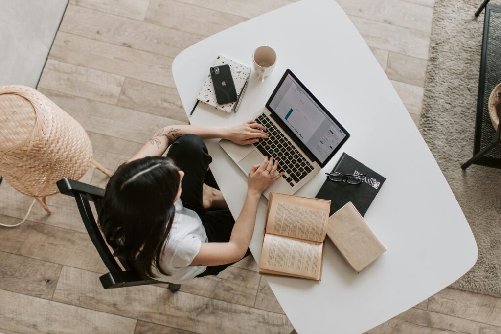 Femme travaille sur une stratégie de transformation digitale sur son ordinateur portable. Sur le bureau il y a un iPhone, une agenda, une tasse de café vide, des livres et des lunettes